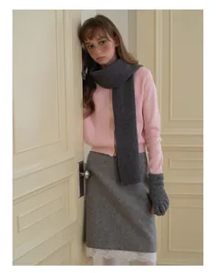 Détail de l'écharpe en tricot gris foncé et des gants sur un cardigan rose doux