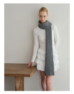 Detail of soft dark grey knit wool scarf texture worn by model in a cozy indoor setting