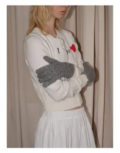 Détail de gants gris en maille torsadée portés avec un cardigan blanc brodé cœur