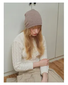 Dettaglio della trama a maglia di un berretto di lana marrone chiaro e cardigan bianco