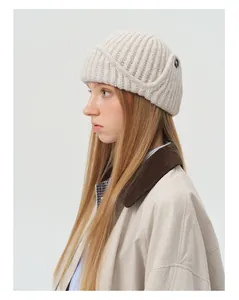 Close-up of cream wool blend knit trapper hat with ribbed texture and button detail