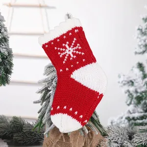 Gestrickter rot-weißer Weihnachtssocken mit Schneeflockenmuster am verschneiten Zweig