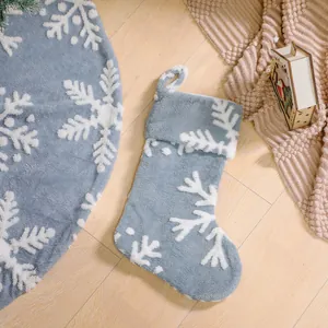 Gray plush Christmas tree skirt and stocking set with white snowflake pattern on wood floor