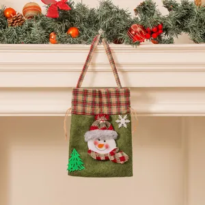 Sac cadeau de Noël vert avec bonhomme de neige accroché sur une cheminée décorée
