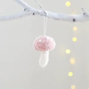Pink wool felt mushroom ornament with white dots hanging on a branch for Christmas decor