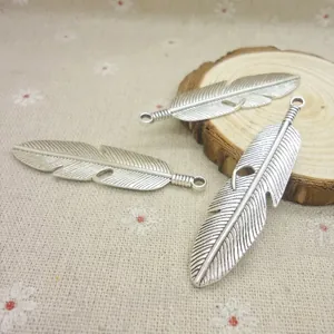 Gros plan de pendentifs plumes en argent antique avec détails gravés sur fond de lin