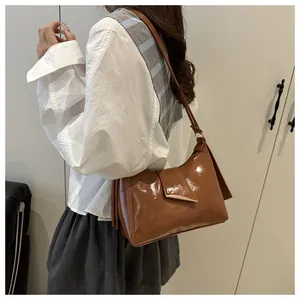 Détail d'un sac porté épaule marron brillant avec boucle dorée et pompons sur le côté