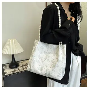 Detail of white tote bag with green butterfly print and braided straps on a model