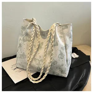 Detail of white tote bag with green butterfly prints and braided faux leather strap