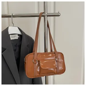 Detail of a brown patent leather shoulder bag with silver hardware on a gray blazer