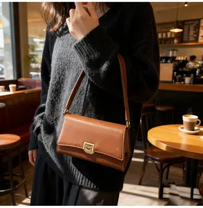 Caramel baguette bag with gold twist lock and slim shoulder strap shown in a cafe setting