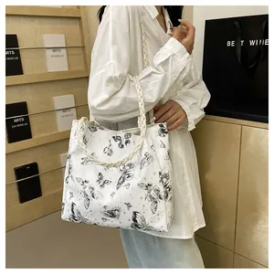 Close-up of white tote bag featuring black butterfly print and woven rope handles