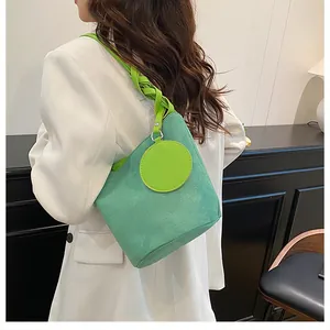 Detail of mint green suede bucket bag with woven strap shown on white suit jacket