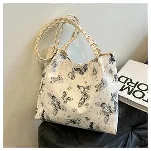 Detail of white tote bag featuring black butterfly prints and braided rope shoulder strap