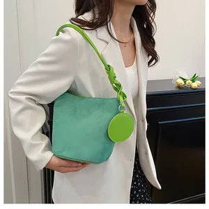 Detail view of mint green suede bucket bag featuring a woven strap and circular pendant charm