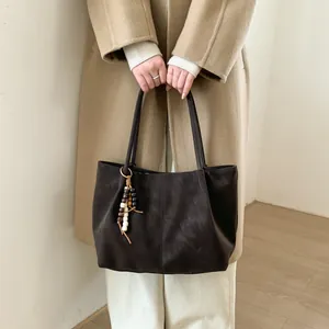 Detail of dark brown matte leather tote bag with unique beaded tassel on camel wool coat