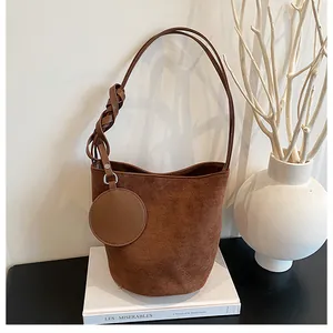 Detail view of brown suede bucket bag featuring woven handle and round coin purse charm