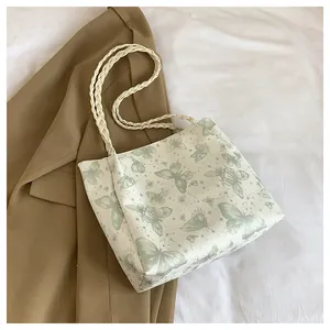 Detail of white tote bag featuring green butterfly prints and beige woven straps