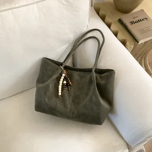 Deep olive green tote bag with wooden bead pendant on a cozy sofa setting
