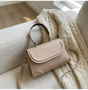 Detail einer minimalistischen beigen Umhängetasche mit goldener Hardware auf dem Sofa