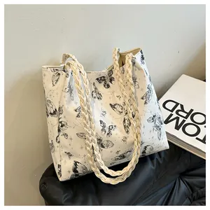 Detail of white tote bag with black butterfly prints and beige woven rope handles