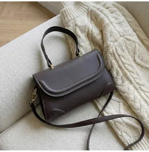 Detail einer dunkelbraunen Ledertasche mit goldener Hardware auf einem Strickpullover