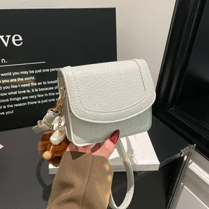 Chic cream white pebble leather crossbody bag with elegant gold buckle and plush charm