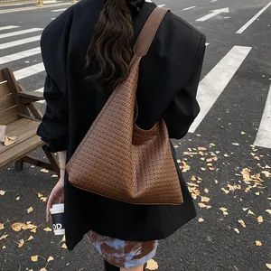 Brown woven hobo tote bag with a wide shoulder strap shown on a street backdrop