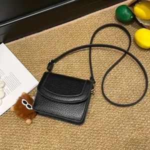 Chic black litchi textured shoulder bag with cute teddy bear charm on textured rug