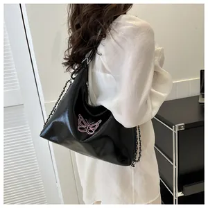 Detail view of black glossy shoulder bag with pink butterfly embroidery on model