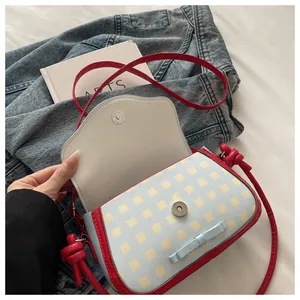 Detail of light blue and yellow plaid crossbody bag with red trim and a bow decoration