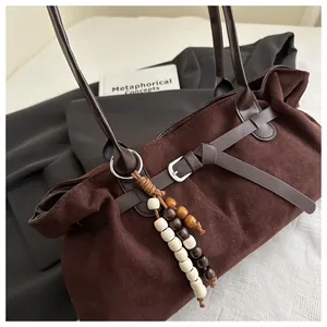 Détail d'un sac cabas en faux daim marron avec lanières en cuir et breloque en perles