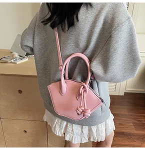 Sac à main trapèze rose avec détail de nœud et bandoulière porté par un mannequin