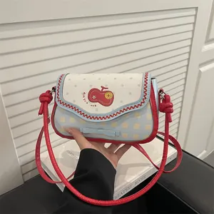 Close-up of small crossbody bag with apple embroidery, polka dots and plaid patterns