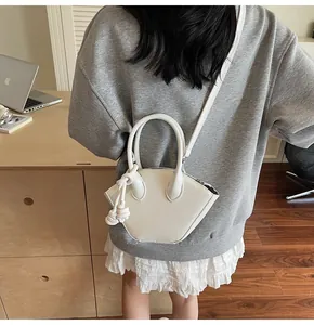 Sac à main blanc forme coquille avec détail pompon présenté dans un bureau moderne
