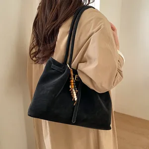 Detail of minimalist black suede tote bag with boho wood bead charm on soft shoulder strap