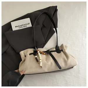 Détail du sac bandoulière en daim beige avec lanières noires et pompon en perles bois