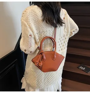 Détail du sac coquillage en cuir caramel avec breloque tissée et bandoulière ajustable