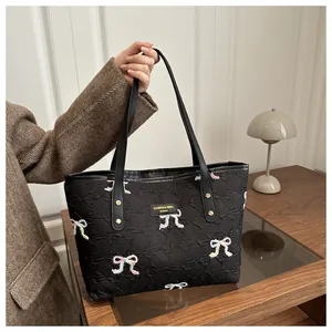 Detail of black quilted tote bag with colorful embroidered bows and gold rivets