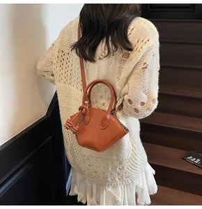 Sac coquille en cuir marron sur escalier en bois montrant son style bandoulière élégant