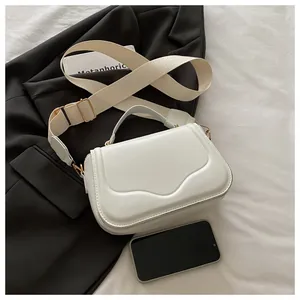 Detail of white saddle bag with wide fabric strap and golden hardware accents