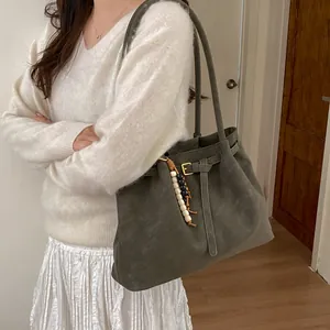 Olive green suede tote bag with buckle strap and wooden bead charm shown on model