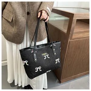 Detail of black quilted tote bag with colorful embroidered bows and metal logo plaque