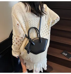 Détail du sac à main noir en forme de coquille avec pendentif à nœud et bandoulière