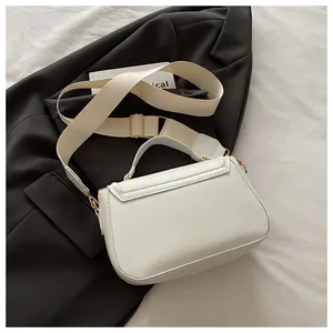 Detail view of cream white saddle bag showing gold hardware and wide fabric strap