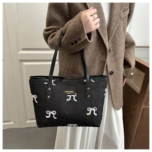 Detail of black tote bag featuring colorful bow embroidery and textured fabric finish