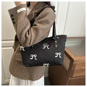 Close-up of black tote bag with sequined bow detail and textured brand plaque
