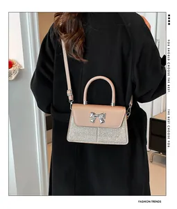 Detail showing the sequined bottom and silver bow on a stylish crossbody bag worn by model