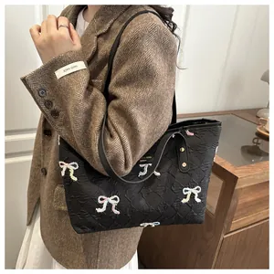 Detail of black quilted tote bag with colorful embroidered bows and leather handles