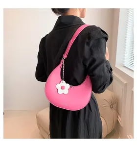 Detailopname van de roze halvemaanvormige schoudertas met witte bloemhanger en merklogo